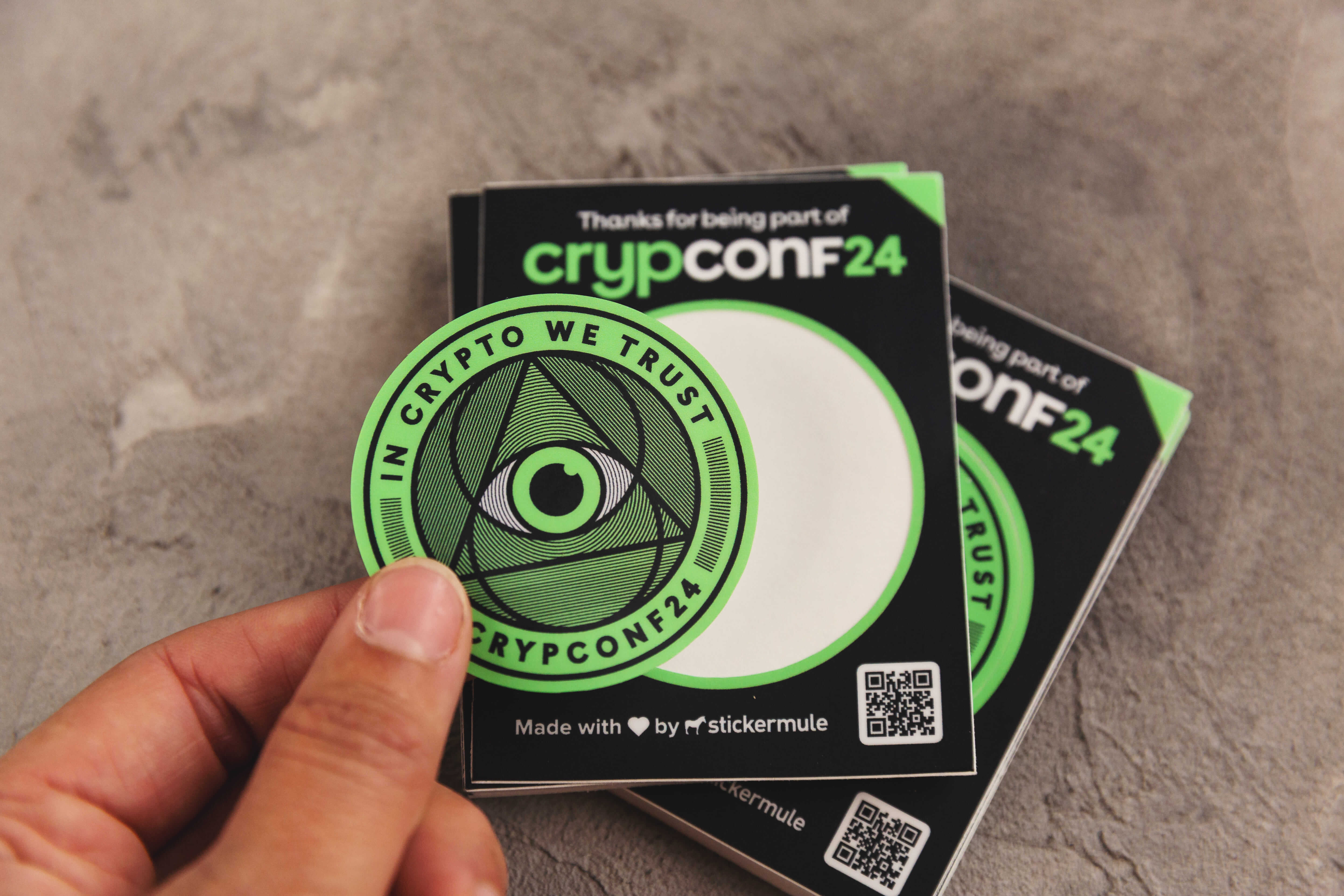 Bright green kiss-cut sticker of crypto business convention, with a hand holding the peeled-off sticker.