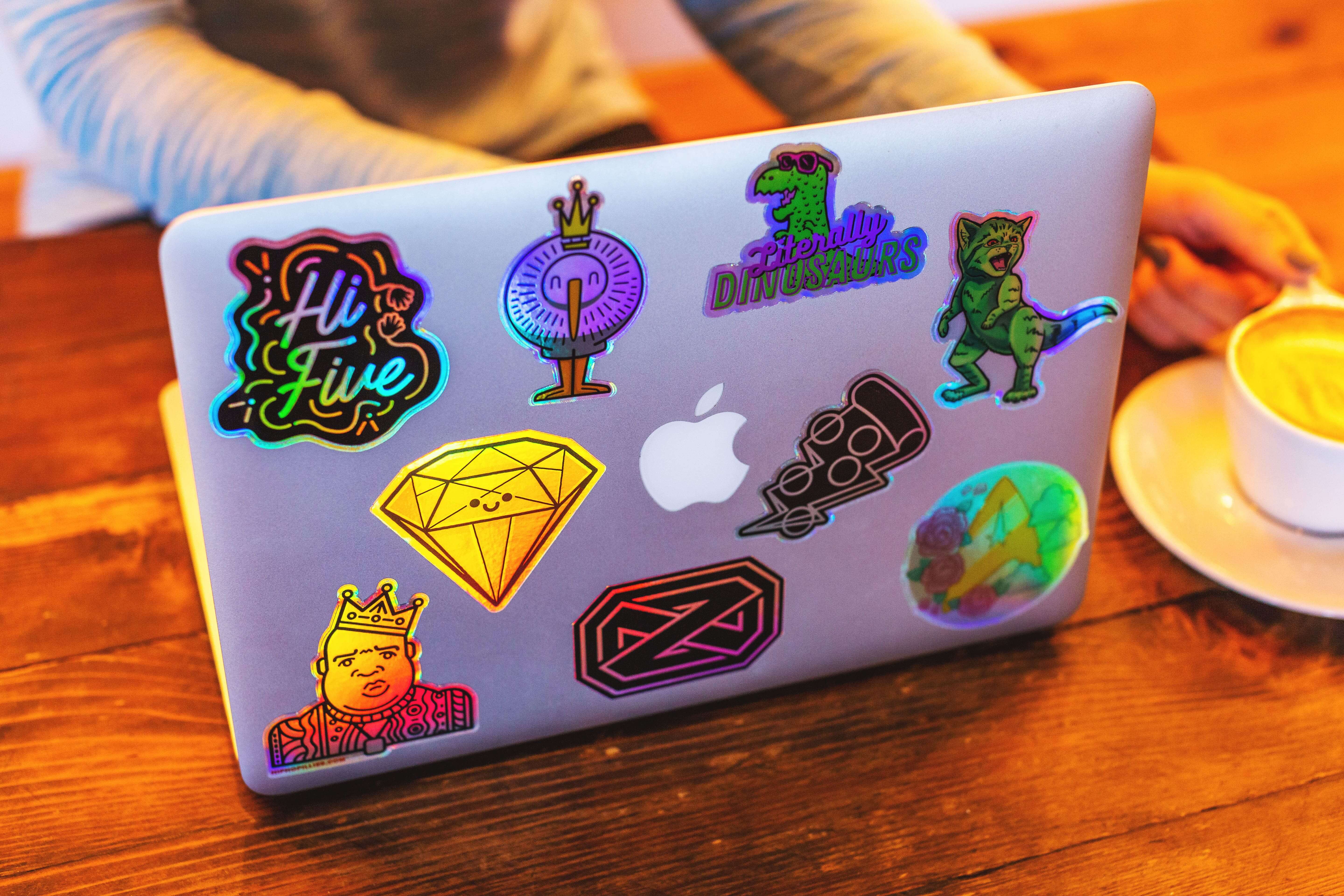Laptop decorated with colorful die-cut stickers, including designs of dinosaurs, crowns, gems, and a holographic High Five sticker.