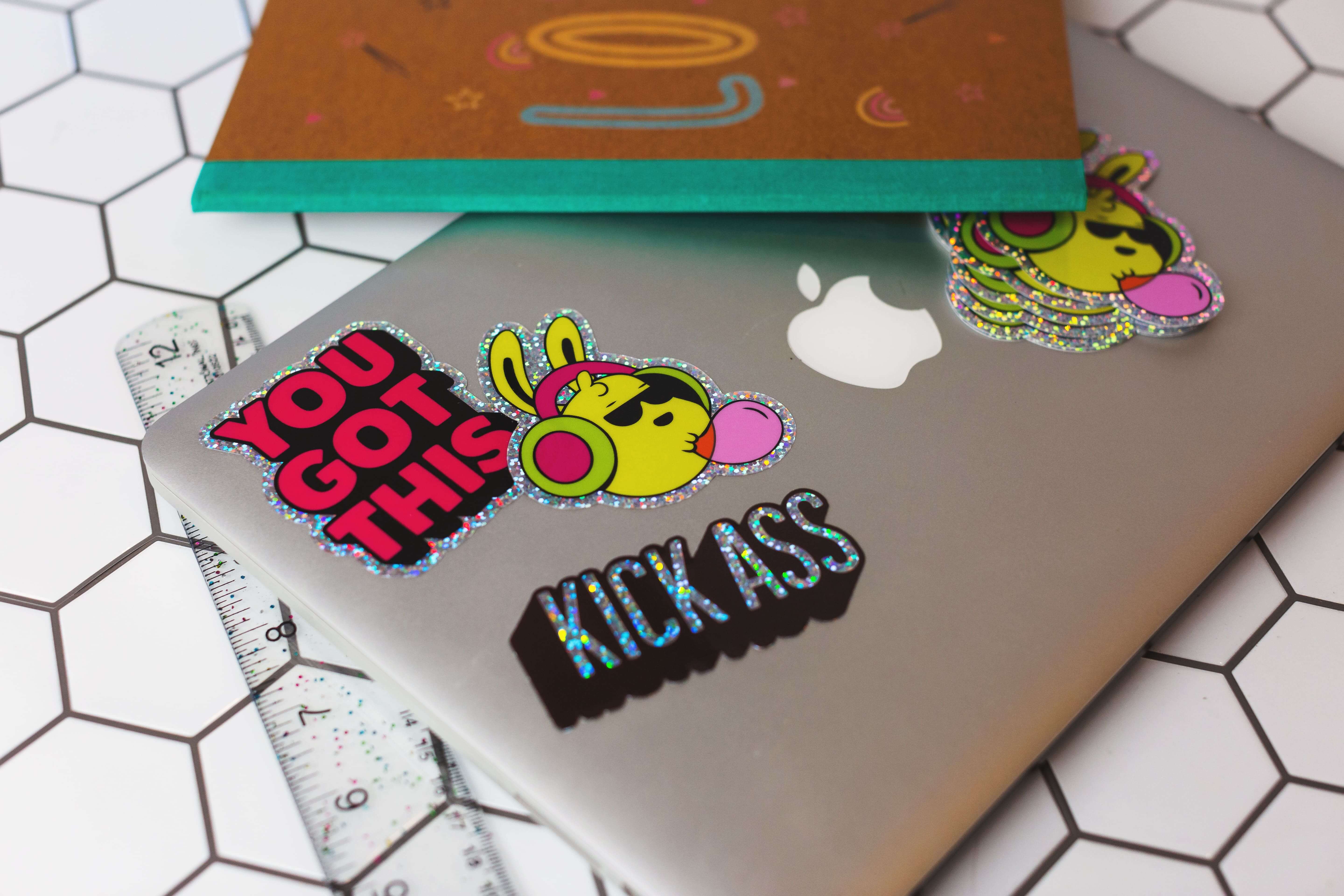 Laptop decorated with colorful holographic die-cut stickers, including typographic designs and bunny characters.