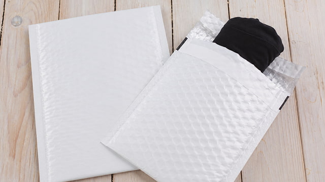 Two white bubble mailers on a light wooden surface. One is fully sealed; the other is open.