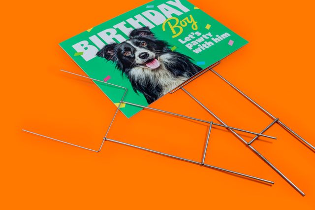 Cartel rígido de cumpleaños de un perro con dos estacas de alambre sobre un fondo naranja