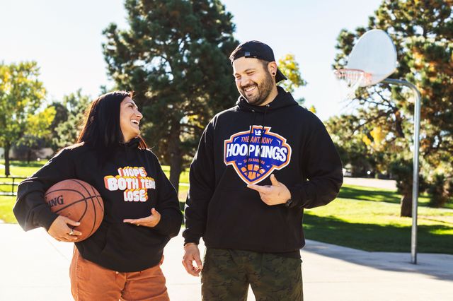 前面にグラフィックが入った黒いパーカーを着た男性と女性が、シンプルな球技コートで会話をしている画像